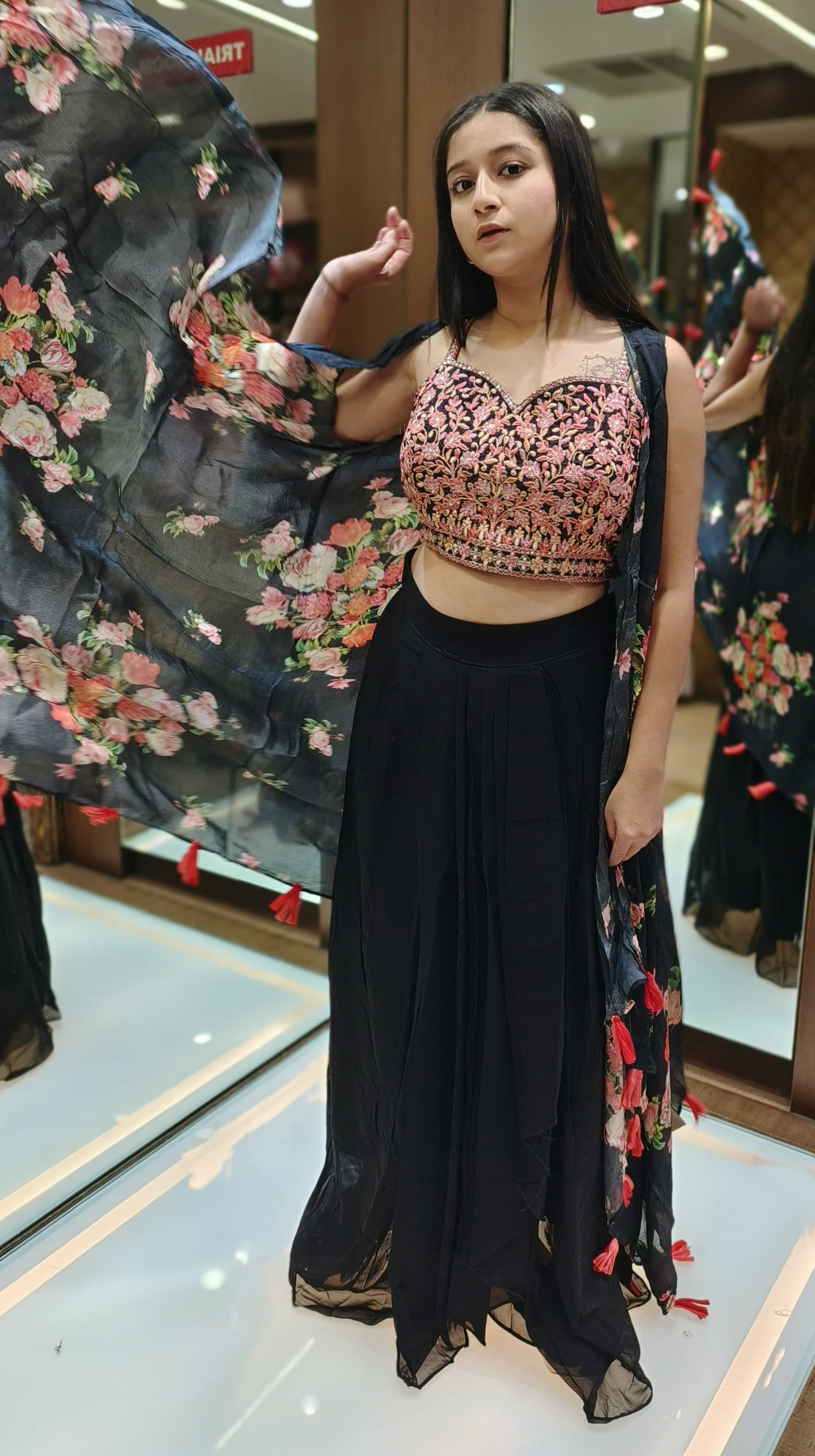 A young woman in a floral top and skirt, radiating happiness while posing in a lush, green environment.