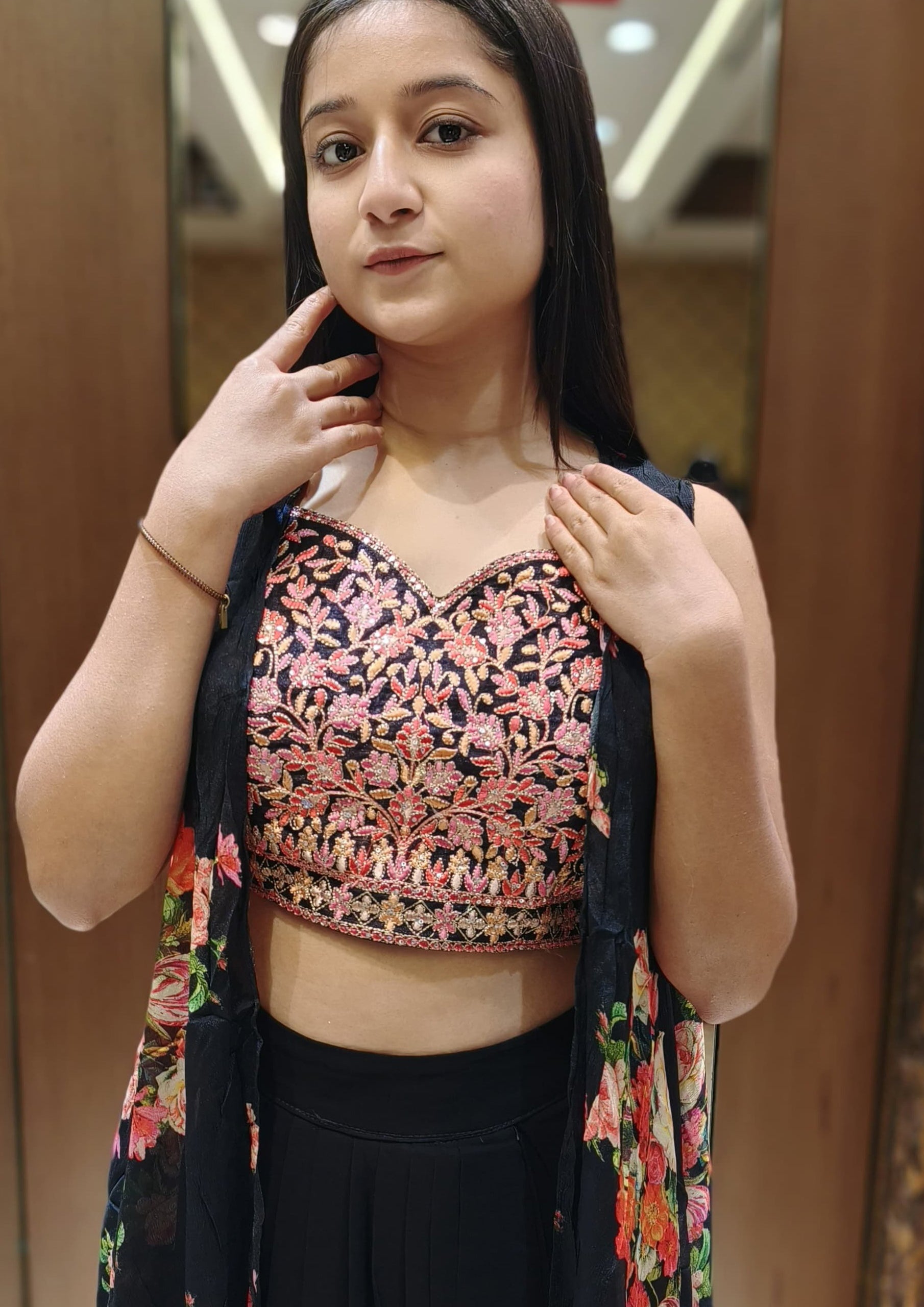 A young woman wearing a floral top and skirt, standing confidently with a bright smile against a natural backdrop.